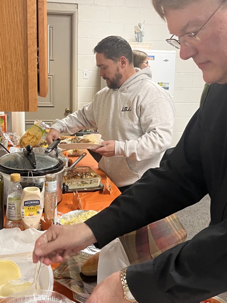 Food layed out on the table people making plates to eat.